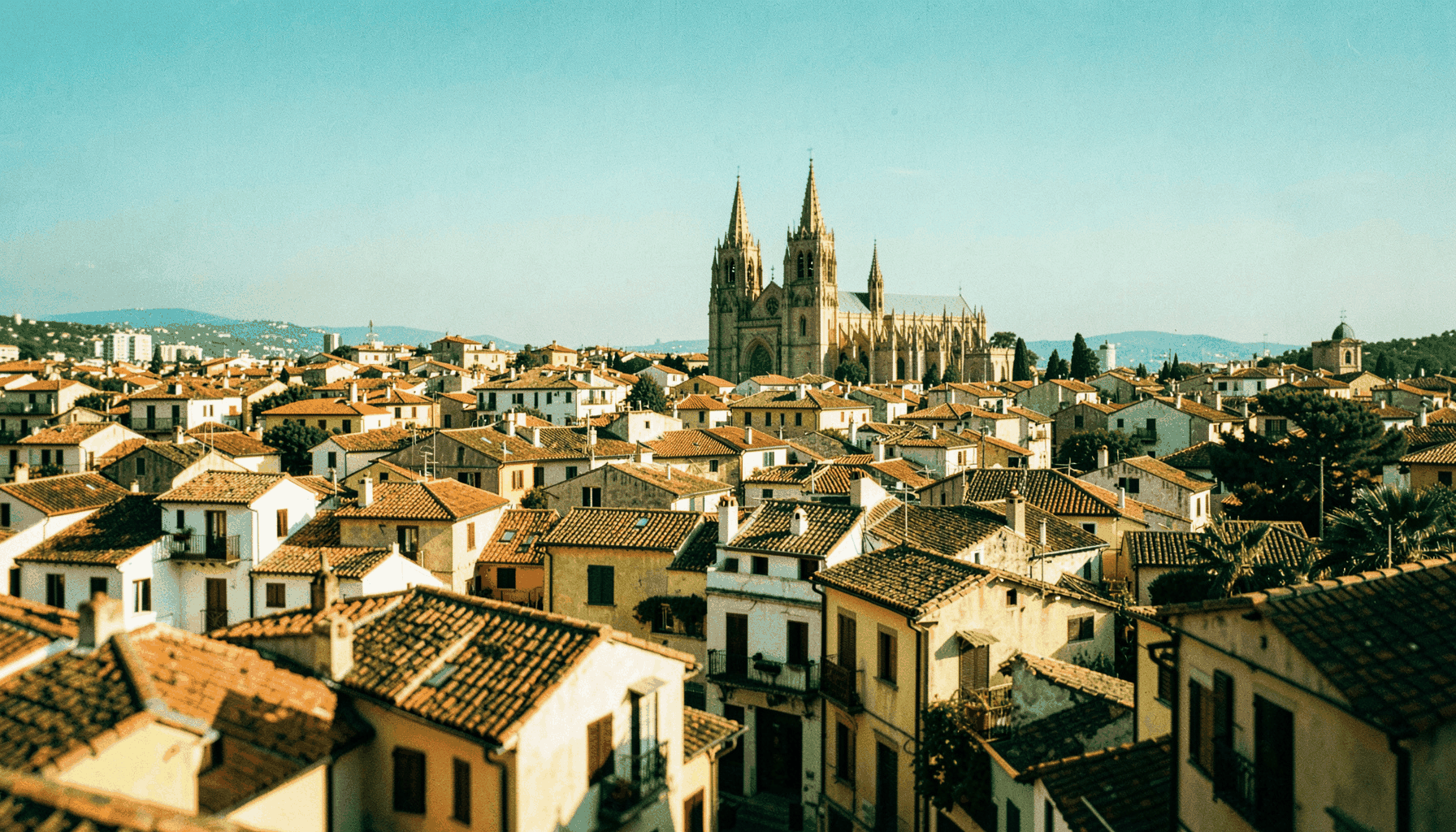 Vista panorámica suave de una ciudad histórica aragonesa con tejados de tonos cálidos y una catedral al fondo bajo un cielo azul claro