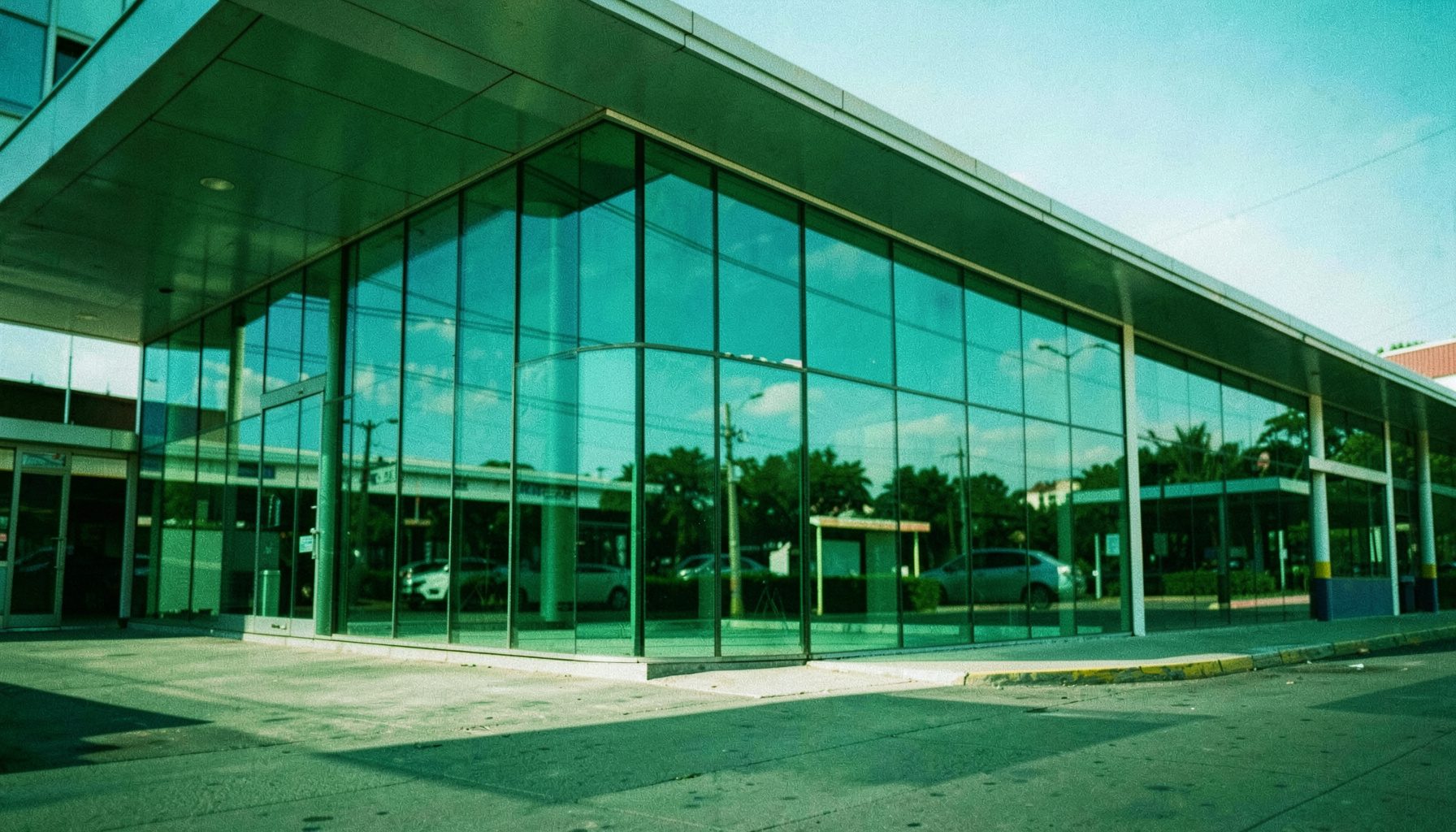 Estación de autobuses moderna con marquesina de cristal reflejando un cielo azul claro